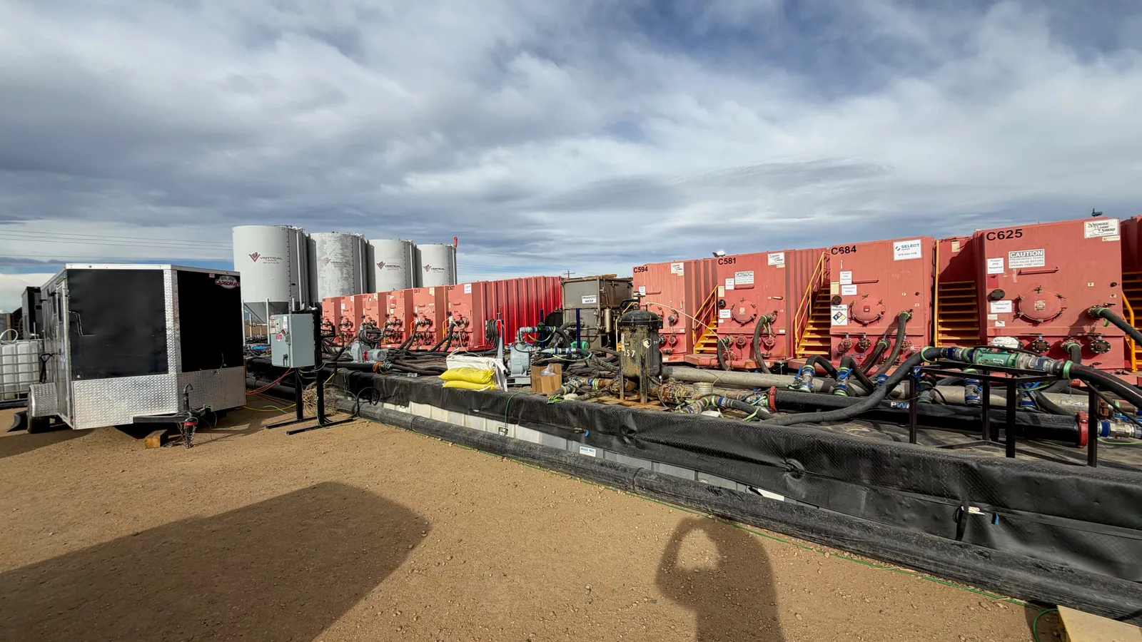 Frac tanks and vertical storage tanks lined up on a PWR location, manifolded together with lay flat hose over lined containment.